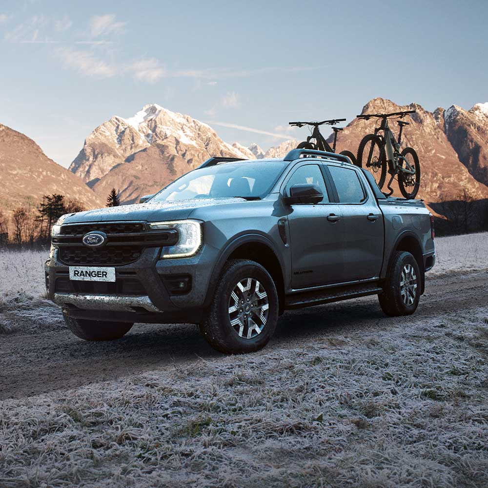 Ford Ranger PHEV in Schwarz. Dreiviertelansicht, fährt mit Fahrradträger über eine verschneite Bergstraße.