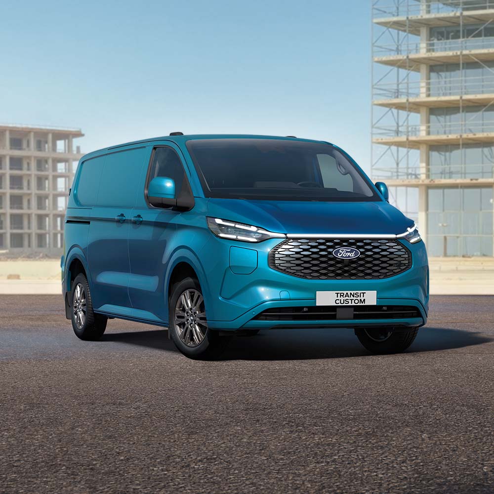 Ford Transit Custom in Blau. Dreiviertelansicht, parkt auf einer Baustelle.