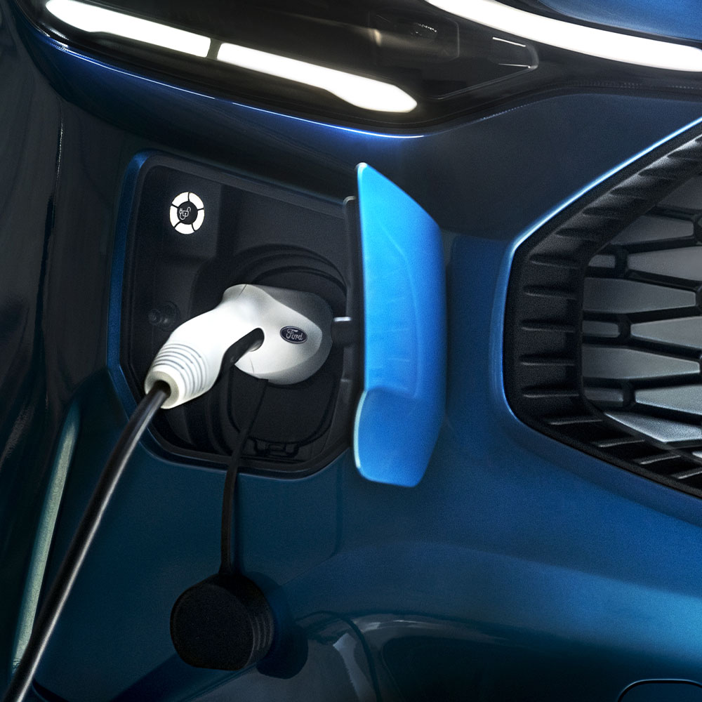 Ein blauer Ford E-Transit Custom lädt mit einem Ladekabel für Elektrofahrzeuge auf.