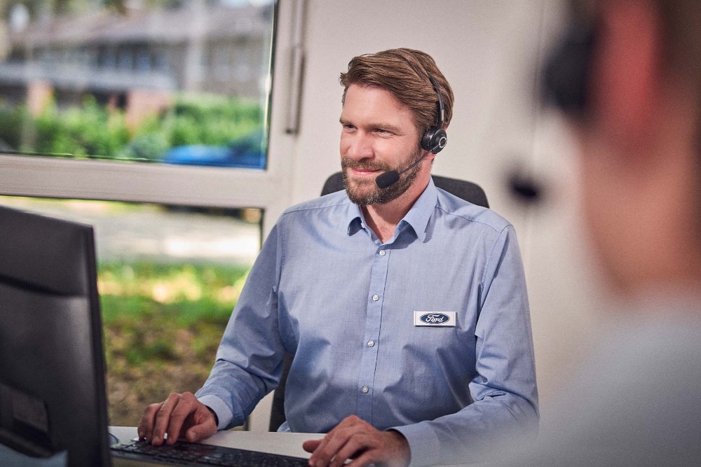 Ford Mitarbeiter sitzt mit einem Headset vor einem Computerbildschirm.
