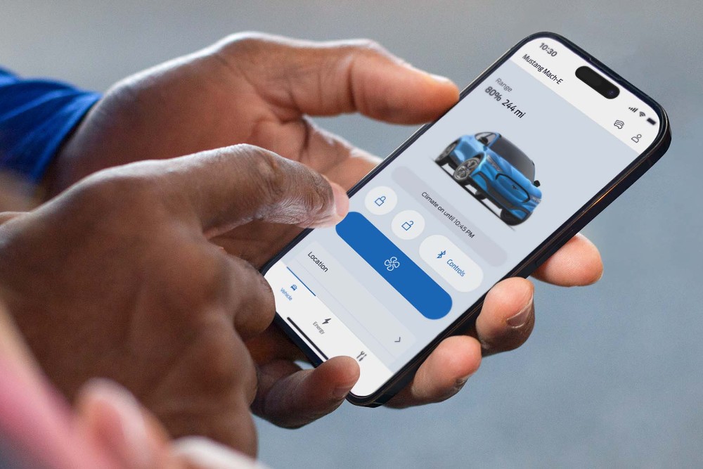 Hand hält ein Smartphone mit geöffneter Ford App, die eine Grafik eines Ford Fahrzeugs zeigt.