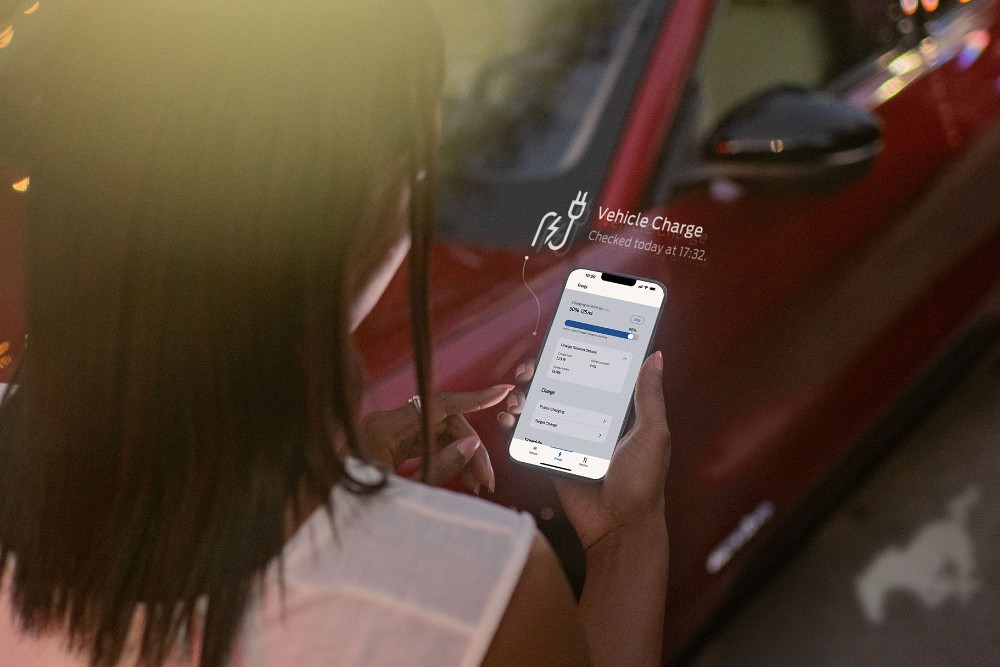 Person prüft den Ladestatus eines roten Ford Elektrofahrzeugs auf einem Smartphone.