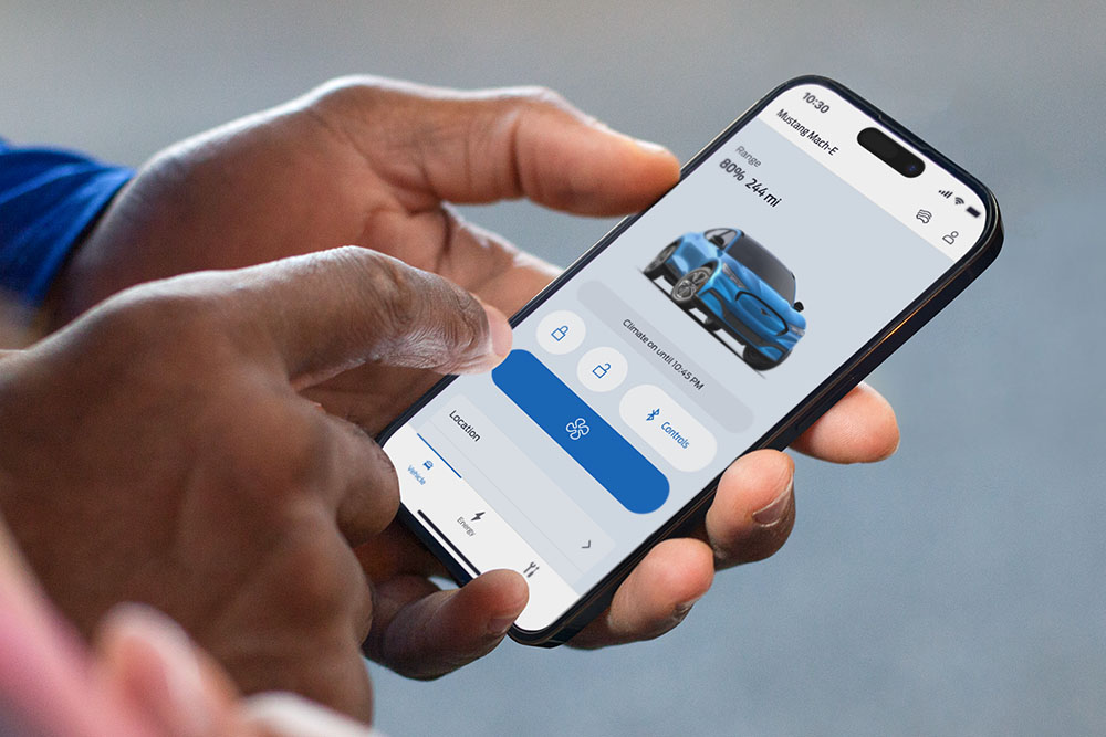 Hand hält ein Smartphone mit geöffneter Ford App, die eine Grafik eines Ford Mustang Mach-E zeigt.