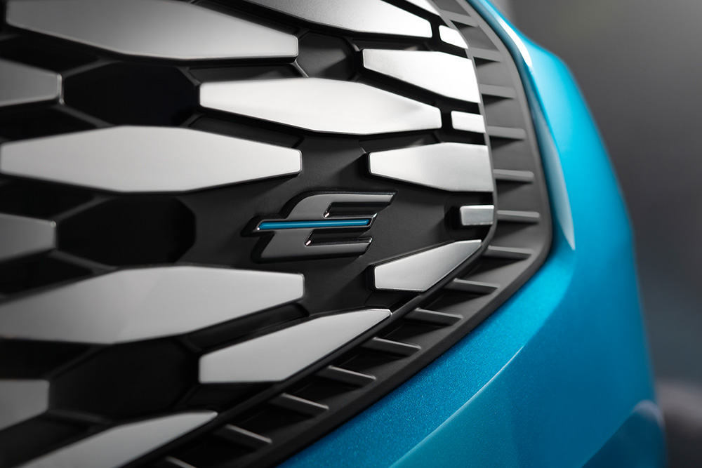 Nahaufnahme des Kühlergrills des Ford E-Tourneo Custom mit dem blauen „E“-Logo für Elektrisch.
