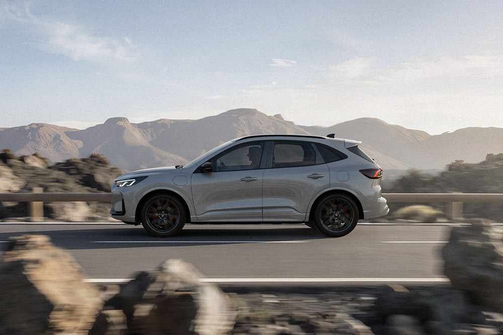 Ford Kuga in Silber. Seitenansicht, bei der Fahrt auf einer Bergstraße.
