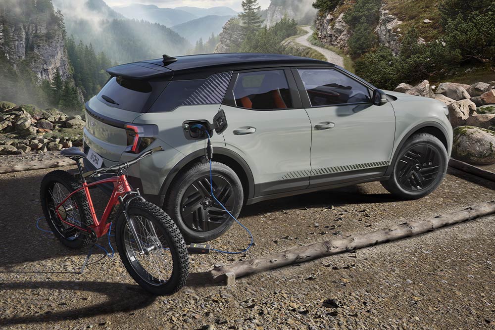 Ein E-Bike wird an einem blauen Ford Explorer aufgeladen, im Hintergrund eine Berglandschaft.