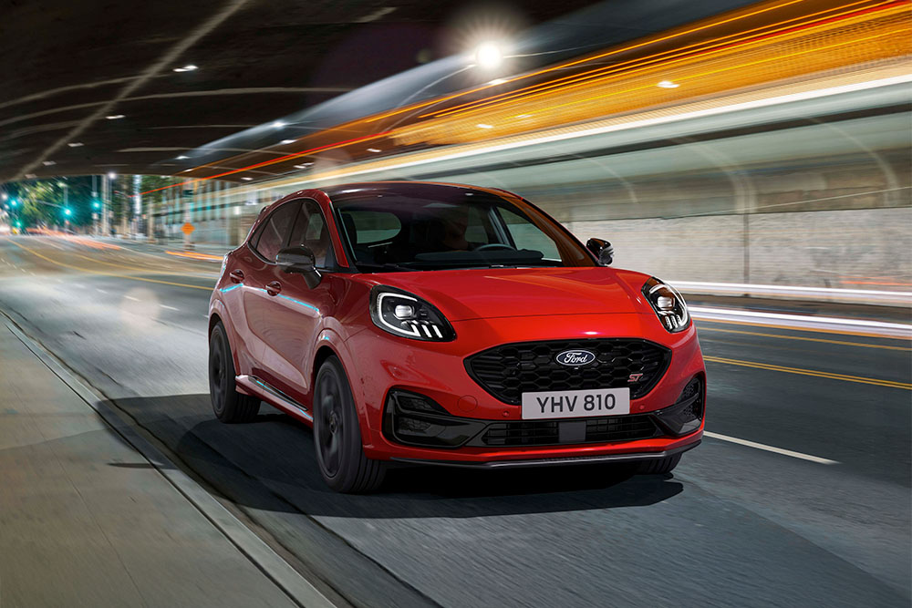Ford Puma ST in Rot. Dreiviertelansicht, fährt in einer Stadt bei Nacht. 