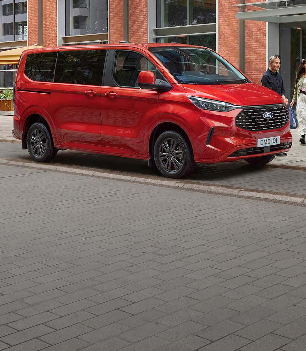 Ford Tourneo Custom in Rot. Dreiviertelansicht, parkend vor einem Gebäude.