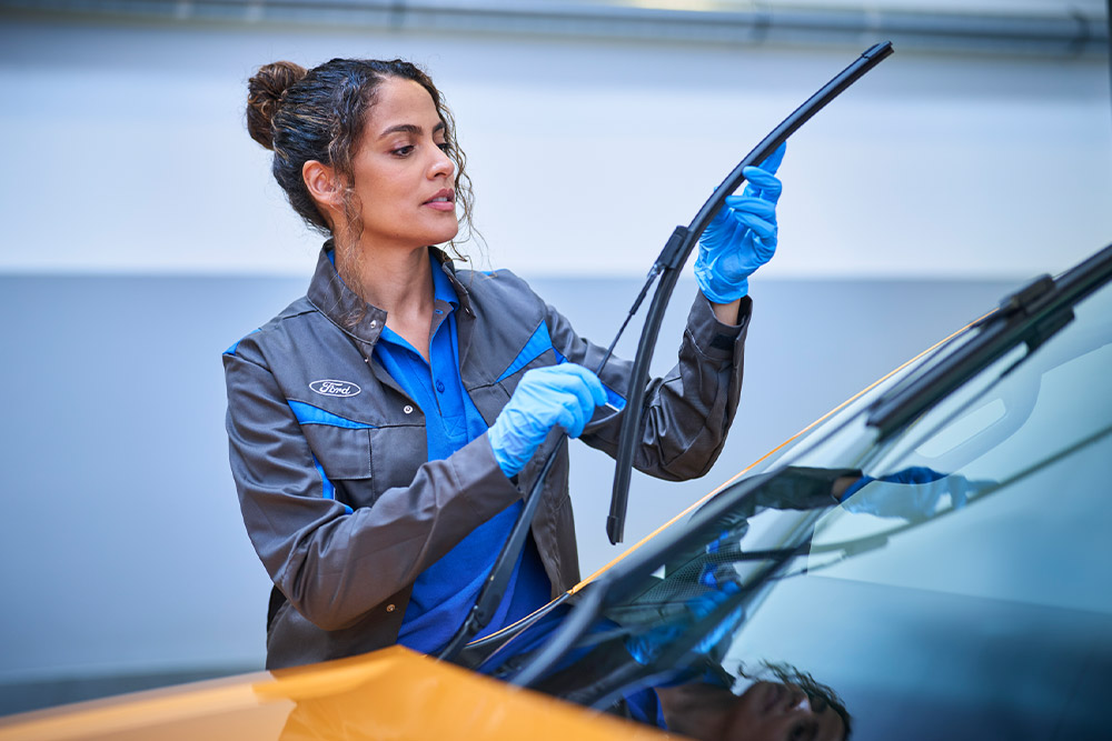 Ein Ford Techniker mit blauen Handschuhen stellt einen Scheibenwischer an einem Fahrzeug ein. 