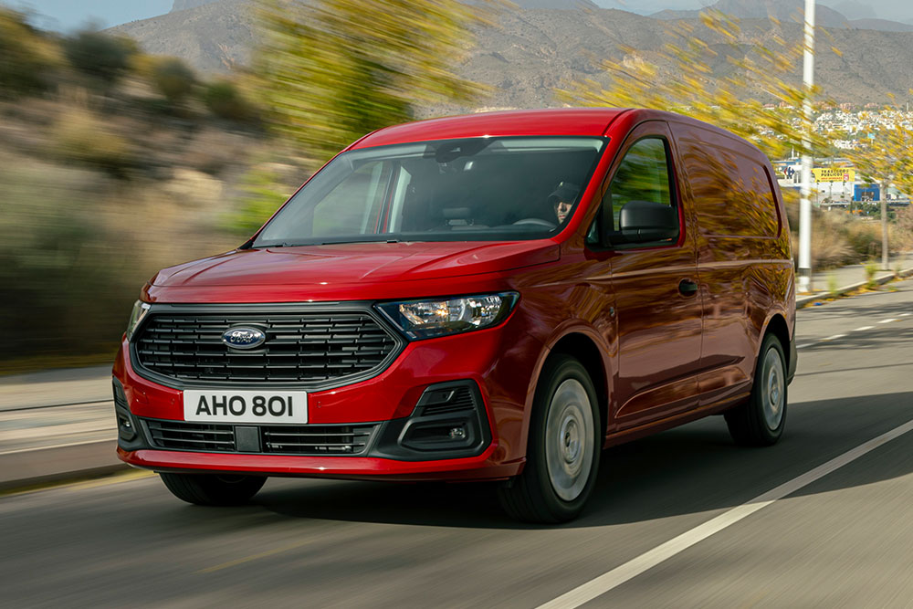 Ford Transit Connect in Rot. Dreiviertelansicht, fahrend auf einer Straße mit Bäumen im Hintergrund.