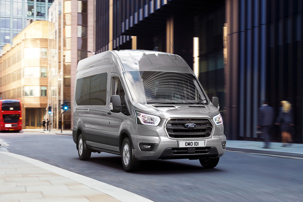 Ford Transit Kombi in Silber. Frontansicht, während der Fahrt durch eine Innenstadt.