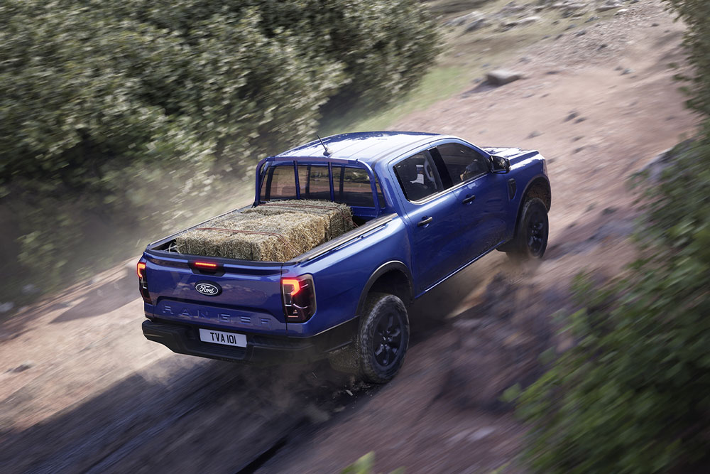 Ford Ranger Plug-in-Hybrid in Blau. Dreiviertelansicht, fährt bergauf auf einer unbefestigten Straße.