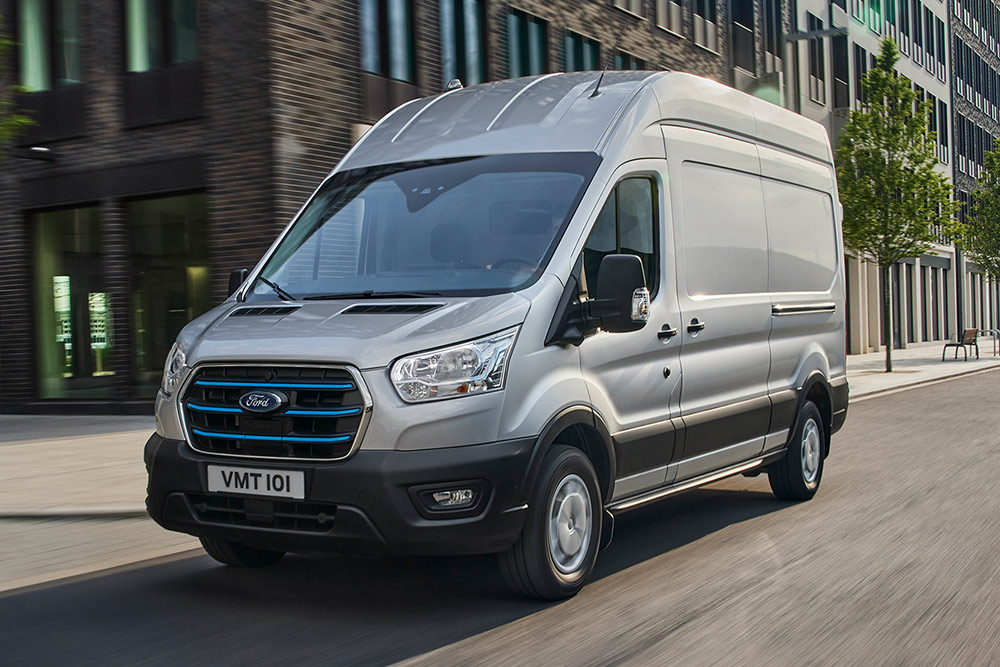 Ein silberner Ford Transit fährt durch eine Stadtlandschaft.