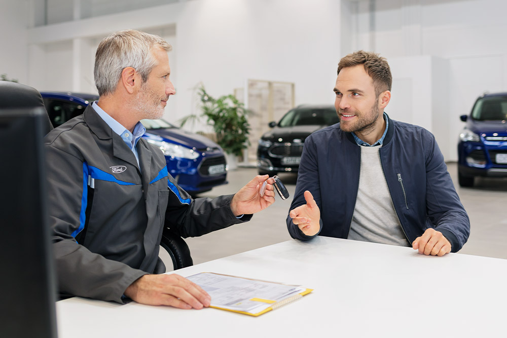 Zwei Männer sitzen sich in einem Ford-Autohaus gegenüber.