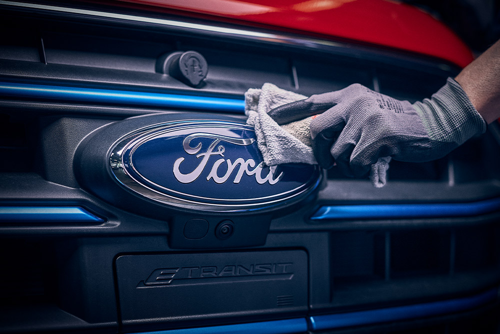  Nahaufnahme eines Technikers, der das Ford-Logo an der Vorderseite eines roten Transporters poliert.