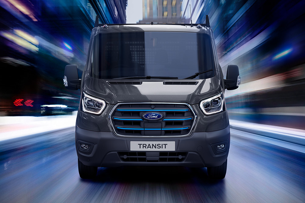 Ford E-Transit in Grau. Frontansicht, fährt auf einer Straße.