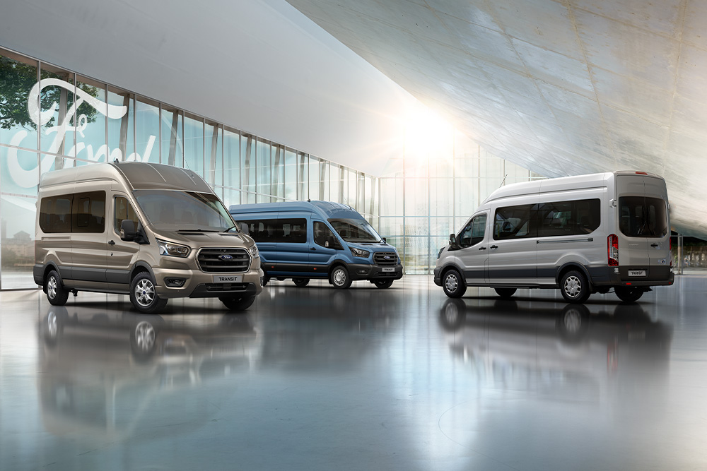Drei Ford-Transporter stehen in einem modernen Showroom mit Glasfassade, das Ford-Logo im Hintergrund.