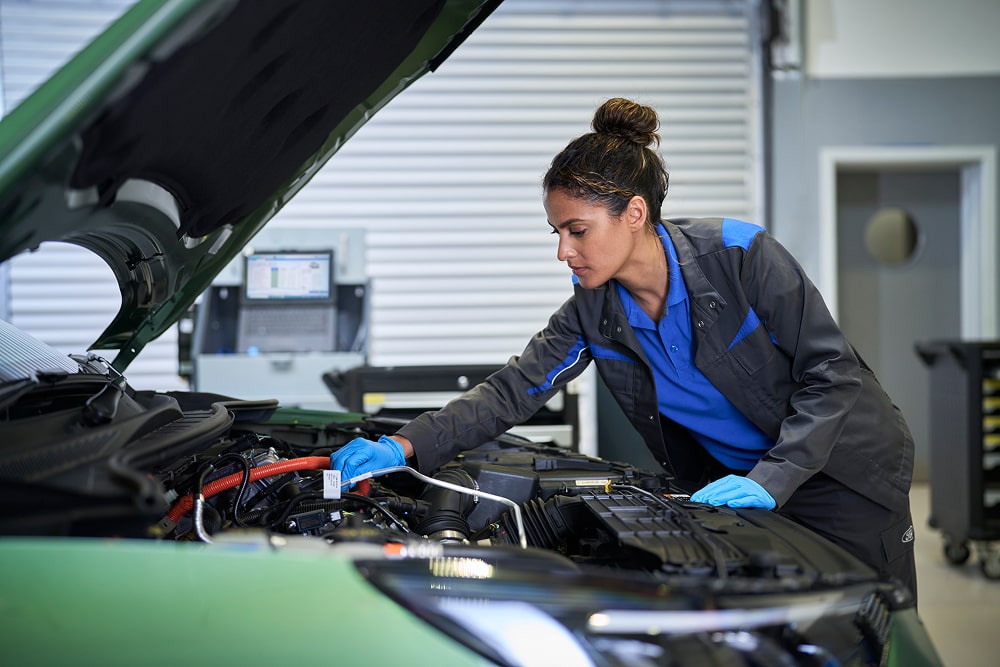 Ein Ford-Mechaniker, der in einer Werkstatt einen Automotor bei geöffneter Motorhaube inspiziert.