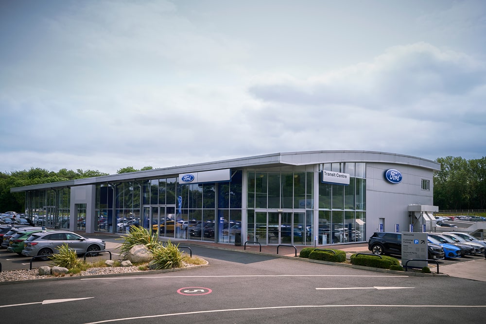 Außenansicht eines Ford-Autohauses mit großen Glasfenstern. Autos stehen draußen.