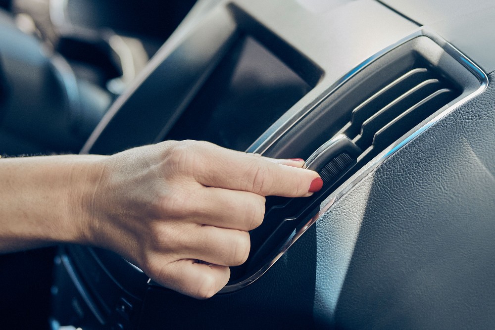 A hand with red nail polish adjusts a car's air vent.