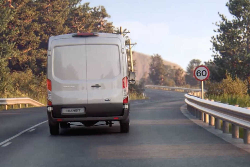 Ford Transit in Silber. Heckansicht, auf einer Landstraße fahrend
